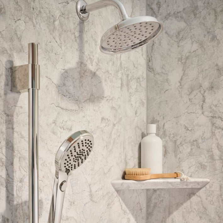 Close up shot of a shower head with a handheld shower head wand. The shower also has a corner shelf with a scrub brush and shampoo bottle on it