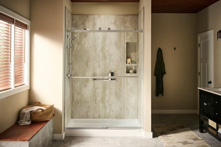 Photo of a bathroom with a focus on the acrylic walk in shower with a sliding glass door and built in shower storage