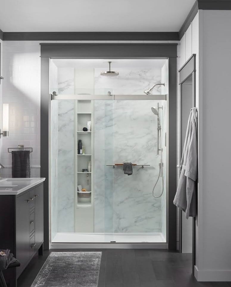 Image of a walk in shower with a glass enclosure, soap niches, a grab bar, and acrylic shower walls