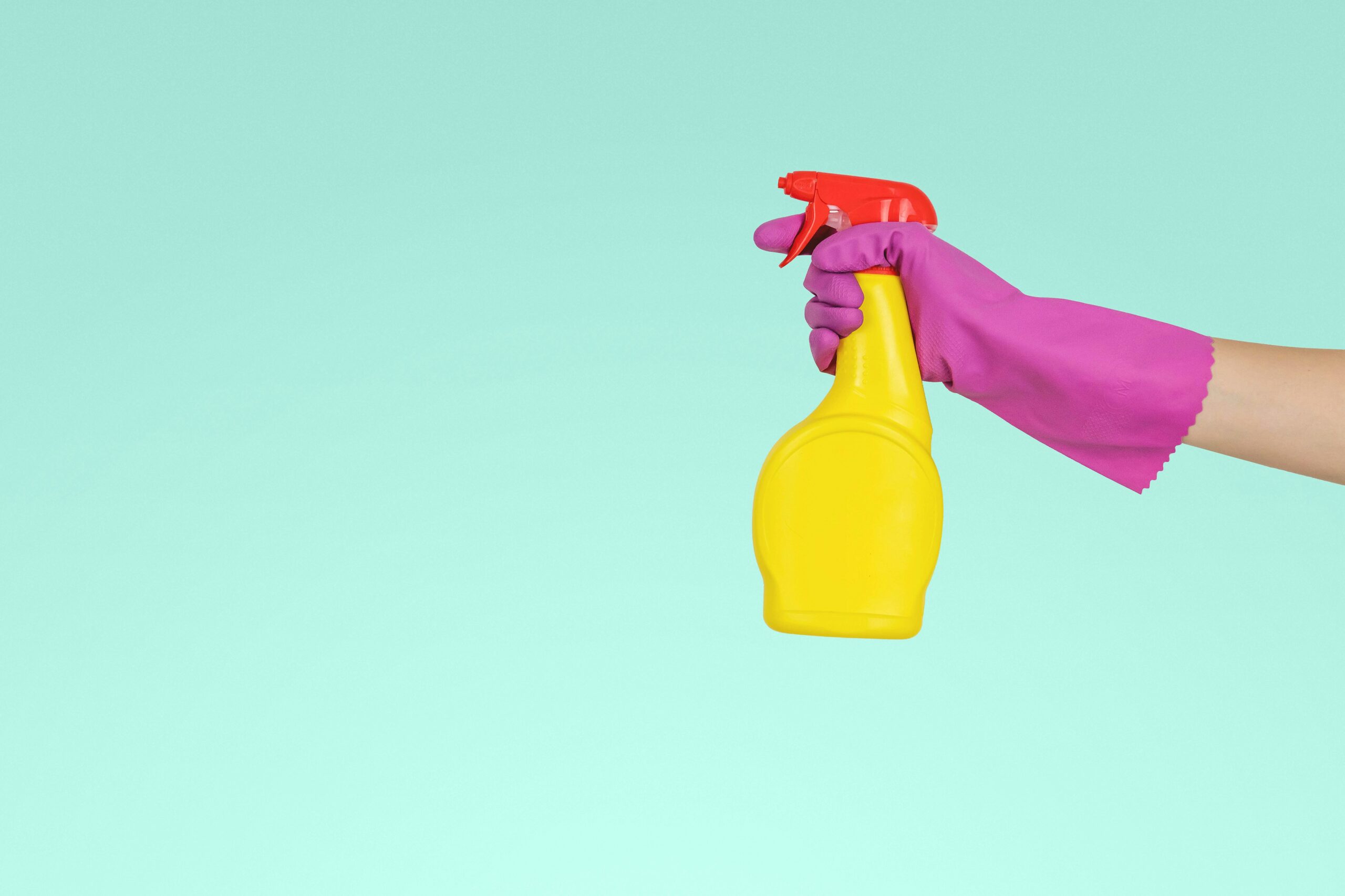 Concept photo of a rubber gloved hand holding a spray bottle of cleaning supplies