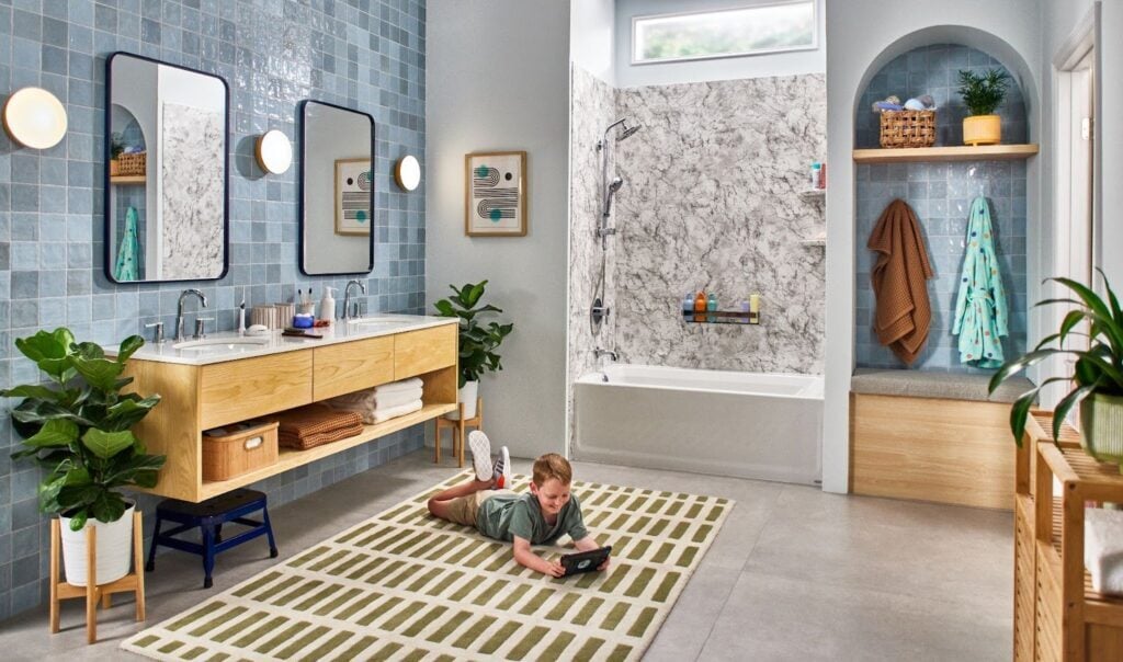 Photo of a child laying on the rug of a large and modern bathroom and looking at a tablet