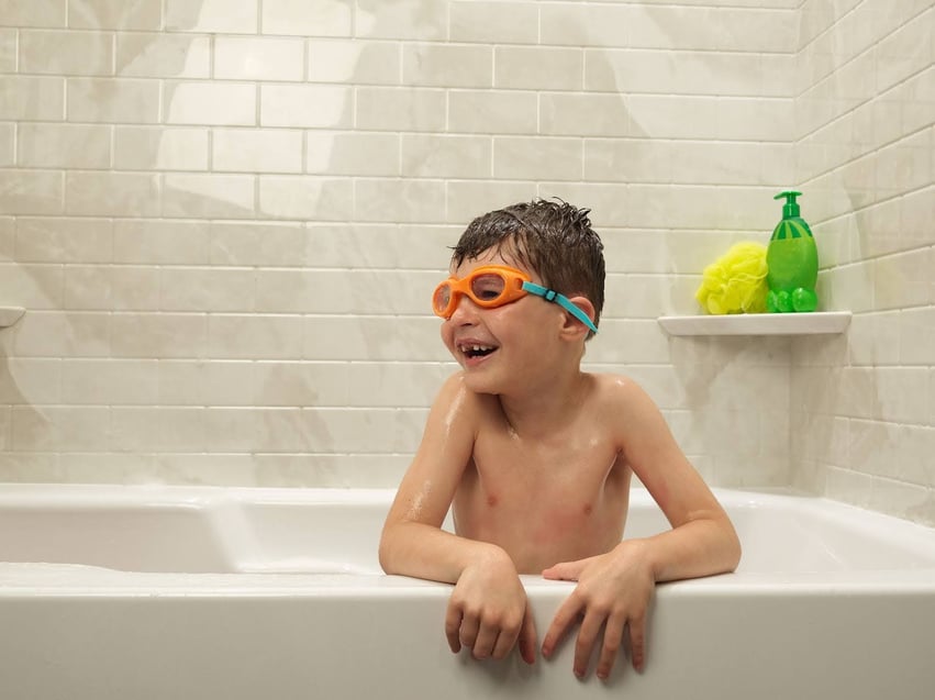 Photo of a kid wearing goggles and playing in an acrylic bathtub shower combo