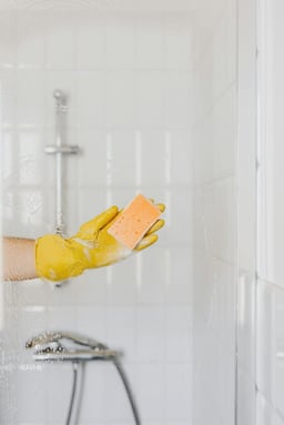 Concept photo of a hand in a rubber glove holding a sponge and washing a glass shower door