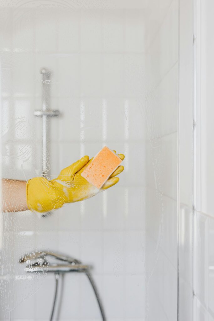 Concept photo of a hand in a rubber glove holding a sponge and washing a glass shower door