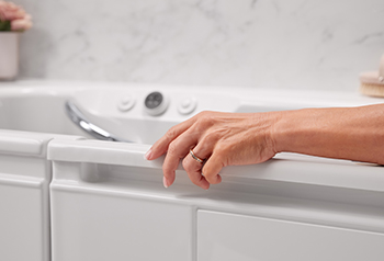 Photo of a hand resting on the side of a walk in bathtub
