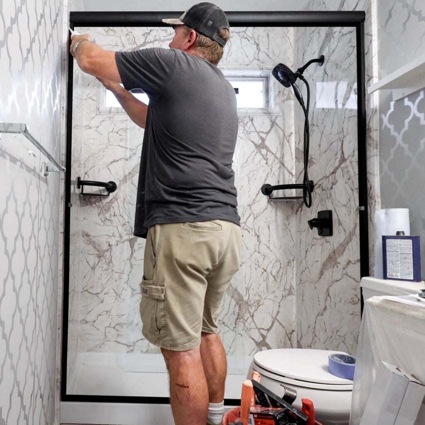 Photo of a ZINTEX installer securing a glass shower door on a deluxe acrylic shower with faux marble walls