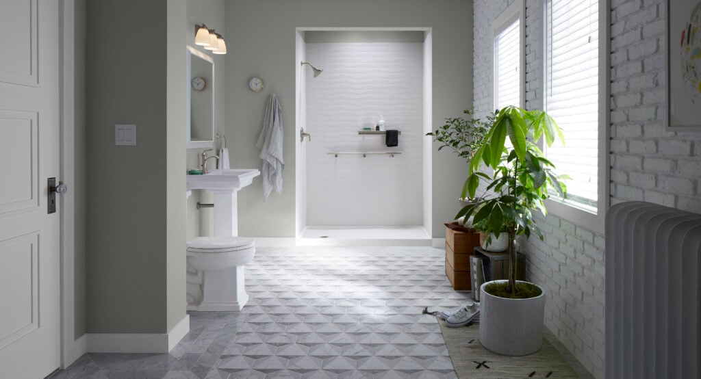Photo of a bathroom with a walk in shower with no door in the distance. You can see acrylic shower walls in a light color with a shelf and grab bar installed