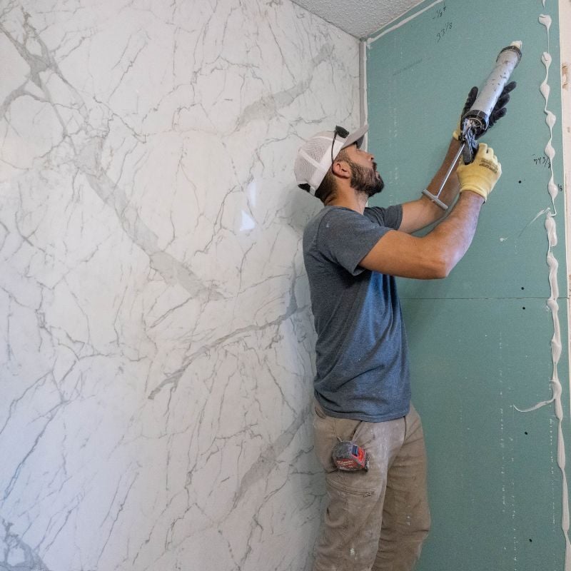 Photo of ZINTEX installer adding adhesive to secure acrylic shower wall panels for a walk in shower