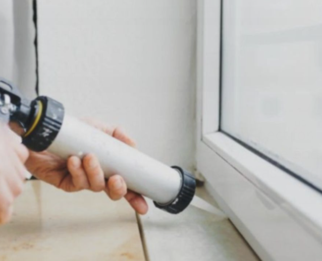 Close up of two hands adding sealant around new replacement vinyl windows