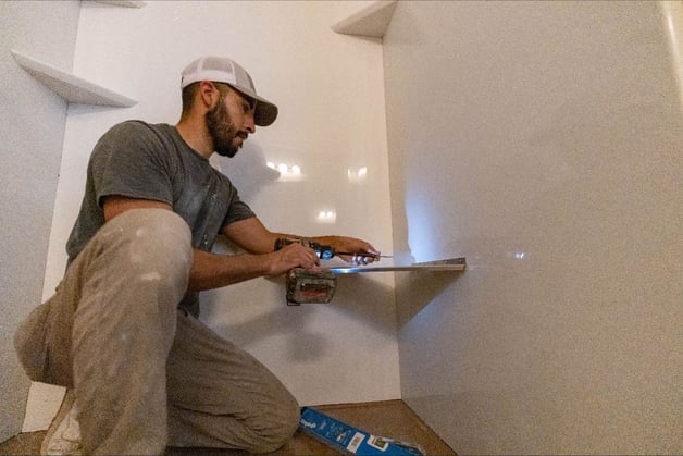 Photo of a ZINTEX installer adding shelves and accessories to new acrylic shower wall panels for shower customization
