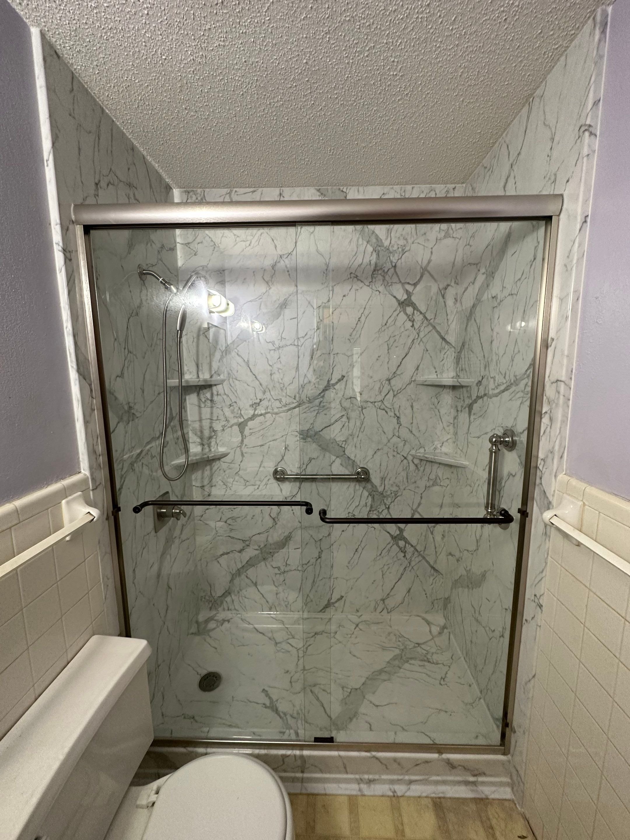 Photo of a walk in shower in a small bathroom. Small bathroom ideas. Acrylic shower with corner shelves and grab bars. Premium acrylic walls.