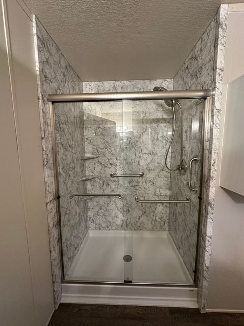 Photo of a walk in shower with a sliding glass door, premium acrylic walls, corner shelves, and a grab bar